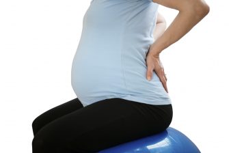 Pregnant woman sitting on fit ball with backache - isolated on white